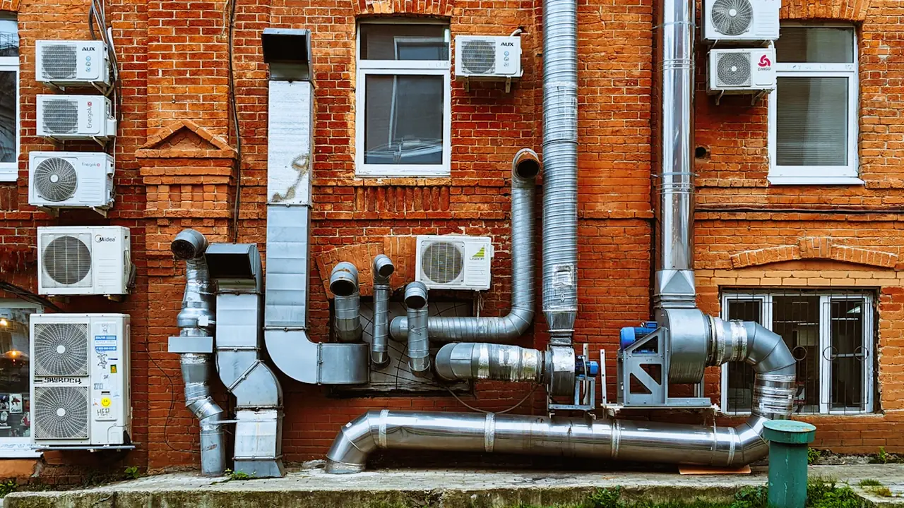 Sarkanas ķieģeļu ēkas fasāde ar daudzām apkures un ventilācijas caurulēm.