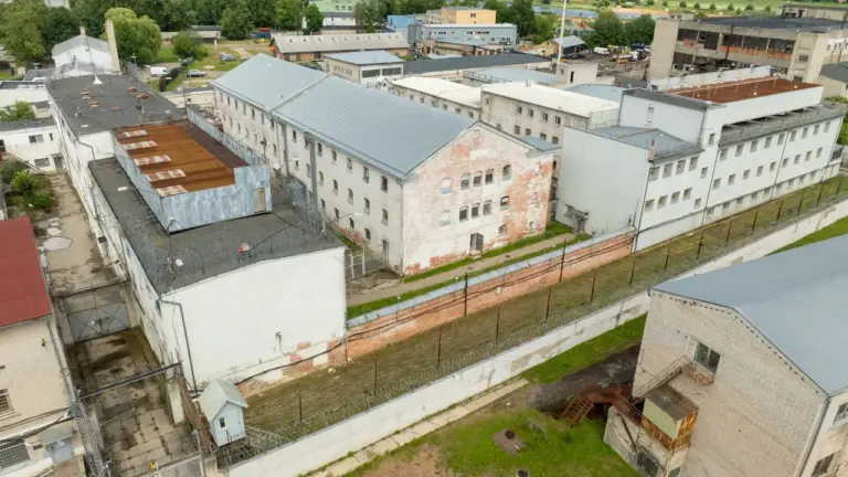 Skats no augšas uz senu cietuma kompleksu ar ķieģeļu ēkām un dzeloņstiepļu žogiem.