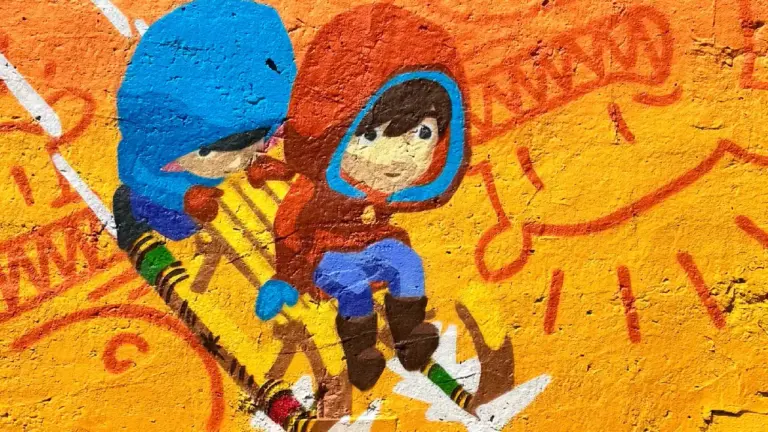 Krāsains grafiti uz oranžas sienas, kurā divi bērni kapucēs brauc ar koka ragavām.