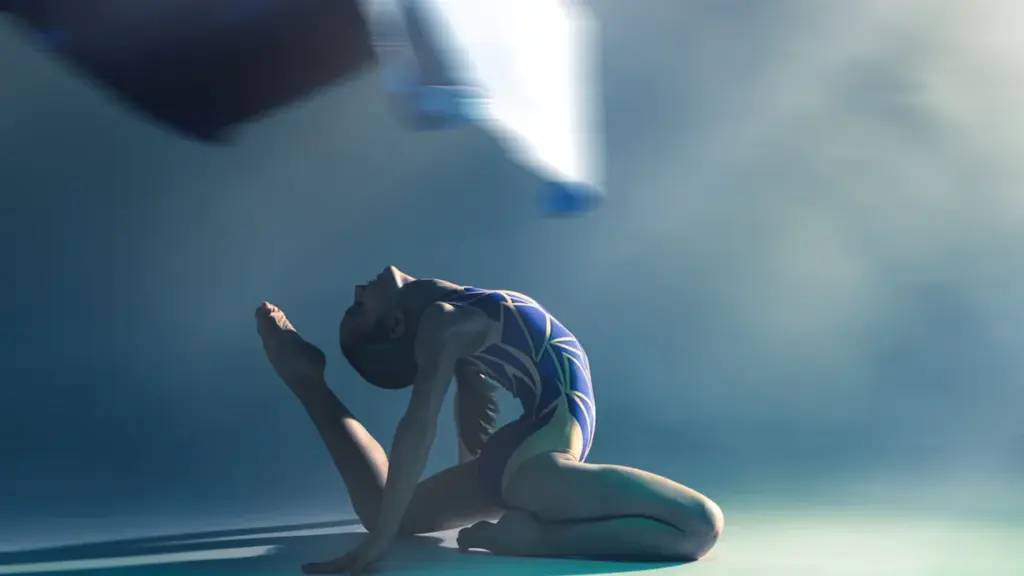 Mākslinieciskās vingrošanas sportiste izpilda elegantu pozīciju studijas apgaismojumā uz zila fona.