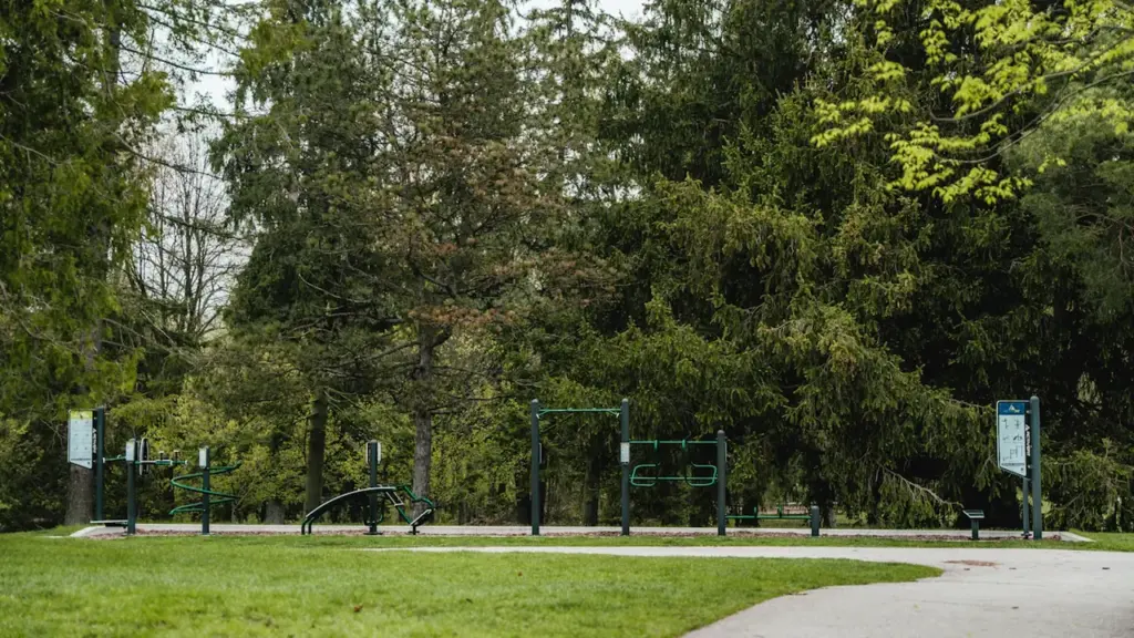 Brīvdabas trenažieri publiskā parkā ar zaļiem kokiem un pastaigu taku Daugavpilī.