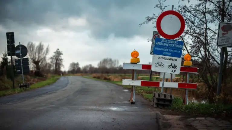 Lauku ceļš ar ceļa zīmēm un brīdinājuma barjerām drūmā, mākoņainā dienā.
