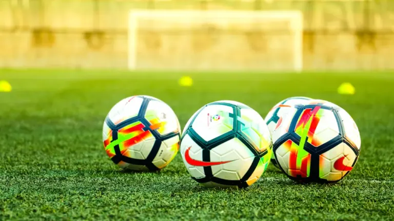 Trīs futbola bumbas uz zaļa futbola laukuma zālāja pirms spēles sākuma.