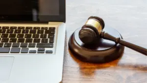 Uz koka galda blakus klēpjdatoram atrodas tiesneša koka āmurs ar misiņa gredzenu.