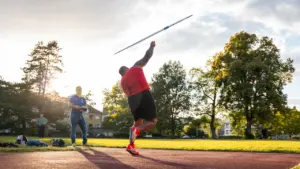 Sportists veic šķēpa metienu vieglatlētikas stadionā saulrieta gaismā, gatavojoties sacensībām.
