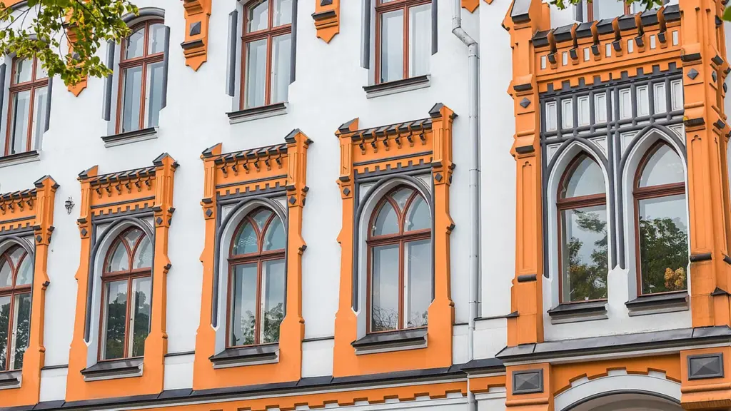 Balta ēka ar oranžiem dekoratīviem elementiem un augstiem arkveida logiem vēsturiskā arhitektūras stilā.