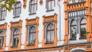 Balta ēka ar oranžiem dekoratīviem elementiem un augstiem arkveida logiem vēsturiskā arhitektūras stilā.